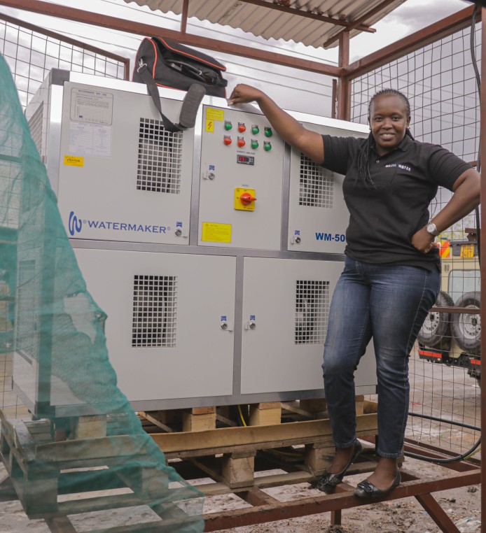 Smiling woman standing proudly next to a air-to-water machine
